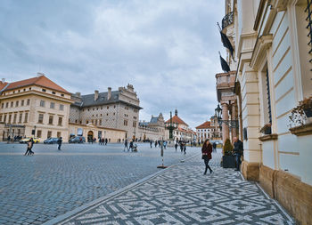 People walking on street amidst buildings in city against sky