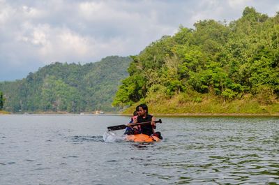 Friends canoeing on river against sky