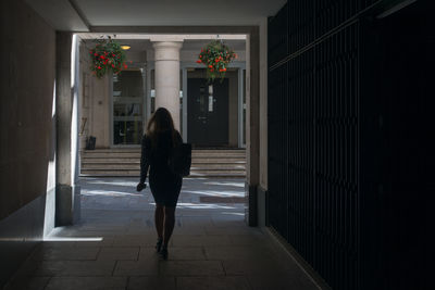 Rear view of professional woman walking in passageway between buildings in the city of london