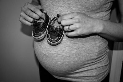 Midsection of pregnant woman holding sandal standing at home