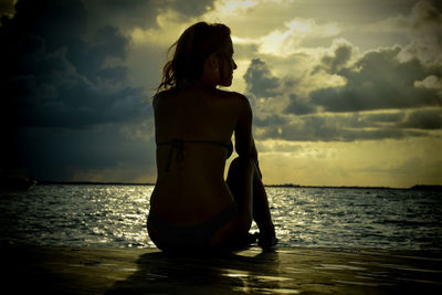 Young woman standing at beach against sky during sunset