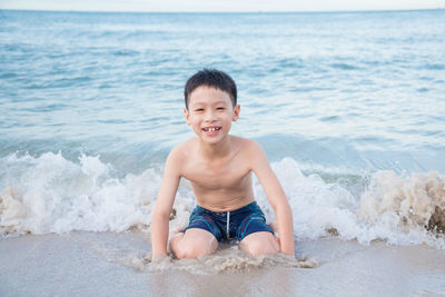 Portrait of shirtless boy kneeling on shore at beach