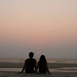 Rear view of people on beach against sky during sunset
