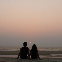 Rear view of couple at beach against sky during sunset