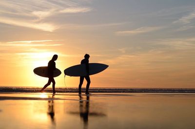 Silhouette people on beach against sky during sunset