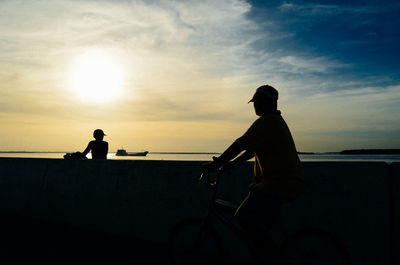 Silhouette men sitting on beach against sky during sunset