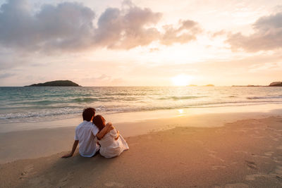 Rear view of couple sitting on beach during sunset