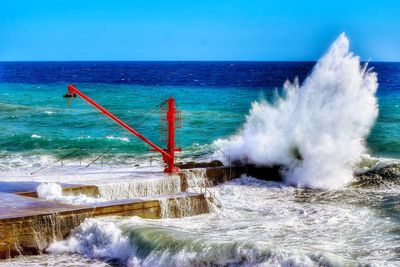 Waves splashing on shore against clear blue sky