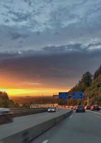 Cars on road against sky at sunset