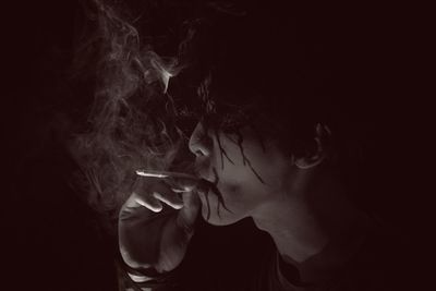 Close-up of man with zombie face paint smoking against black background