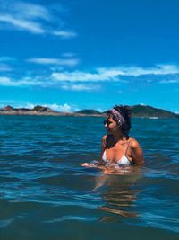 Smiling bikini woman swimming in sea against blue sky