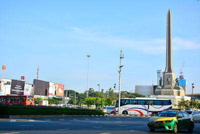 Cars on road by buildings against blue sky