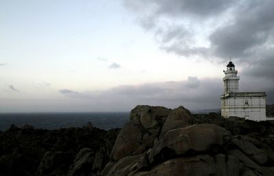 Lighthouse on cliff by sea against sky