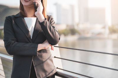 Midsection of businesswoman talking over smart phone while standing by railing