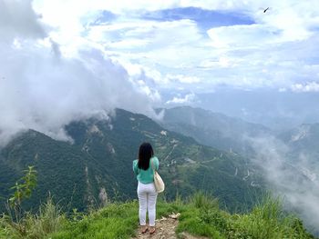 Rear view of woman standing on mountain against sky