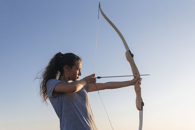 Woman practicing archery by clear sky