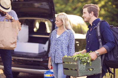 Man carrying wooden crate standing with friends by car