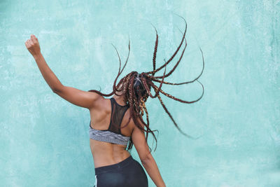 Woman with braided hair dancing against blue wall