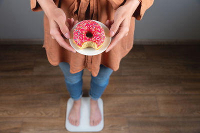 Diet. a woman measures body weight on a scale, holding a donut on a plate. sweets, unhealthy junk