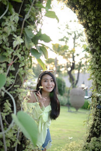 Portrait of smiling young woman standing by tree