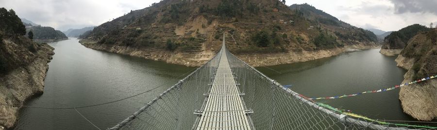Panoramic shot of footbridge amidst mountains against sky