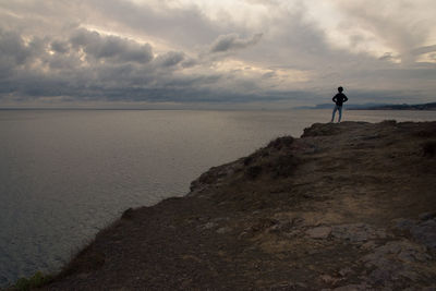 Rear view of teenager boy standing at cliff looking at sea