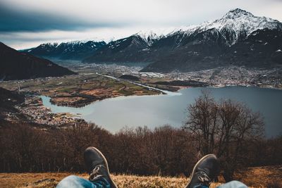 Low section of man against lake and snowcapped mountains