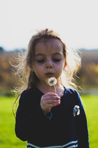 Close-up of girl blowing dandelion against sky