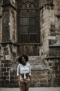 Smiling woman with hands in pockets standing against barcelona cathedral, barcelona, spain