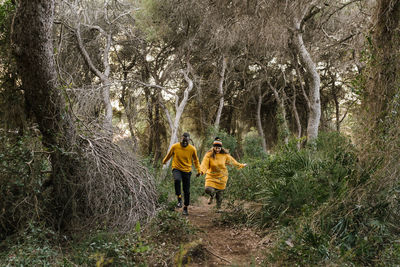 Couple holding hands while running on forest path