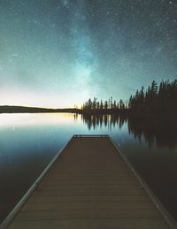 Pier over lake against star field