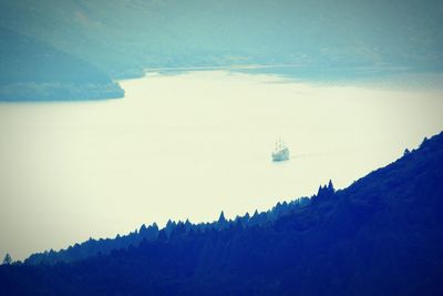 Boat sailing on sea by mountain against sky