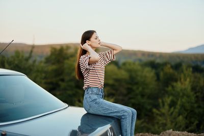 Side view of young woman using mobile phone while standing against sky