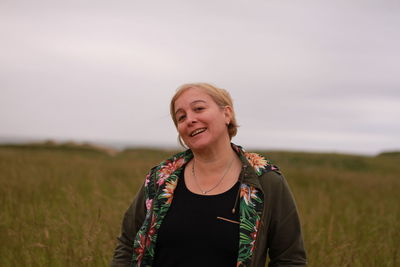 Portrait of smiling young woman standing on field against sky