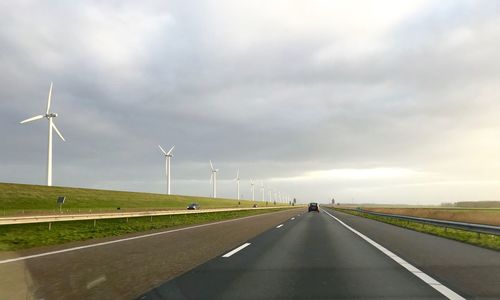 Road by wind turbines against sky