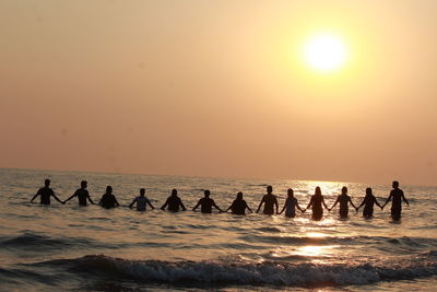 Silhouette people on beach against sky during sunset