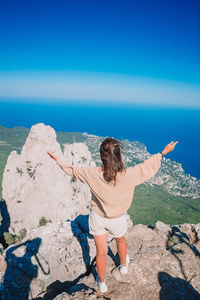 Woman standing on rock against blue sky