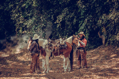 Men wearing hat standing with horse at forest