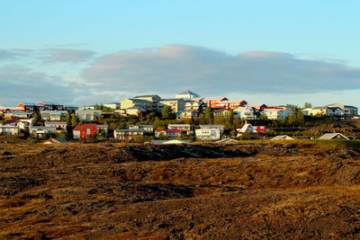 Houses on field by buildings against sky