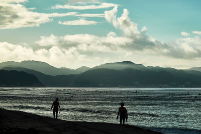 Silhouette people at beach against sky during sunset