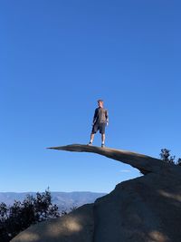 Low angle view of man standing on mountain against clear blue sky