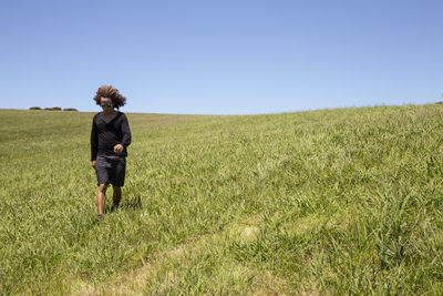 Rear view of woman walking on field against clear sky