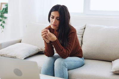 Young woman using phone while sitting on sofa at home