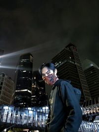 Low angle view of man standing at illuminated modern buildings in city at night