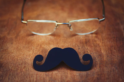 High angle view of eyeglasses and artificial mustache on wooden table
