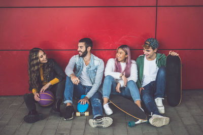 Full length of young couple sitting against wall