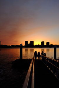 Silhouette people by sea against sky during sunset