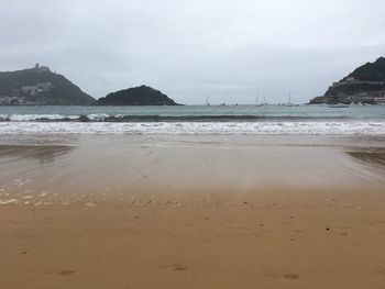 View of calm beach against cloudy sky