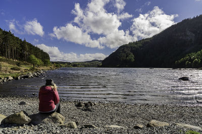 Rear view of woman sitting on mountain against sky