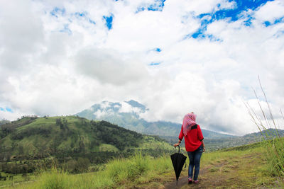 Rear view of woman standing on land against cloudy sky